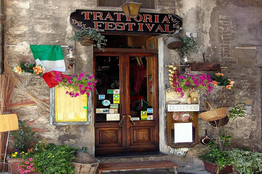 Foto de uma fachada discreta de uma trattoria em uma rua secundária na Itália, com um menu escrito à mão na porta.